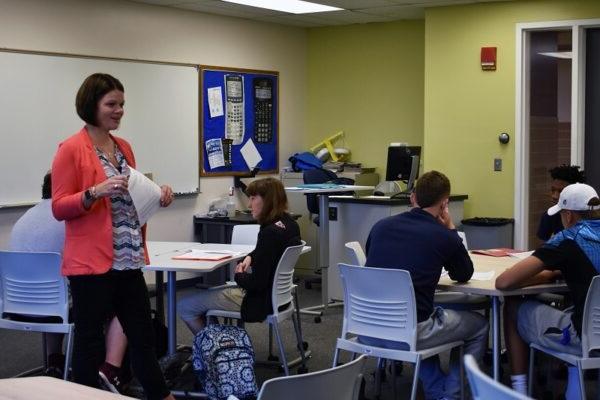 Associate professor walking in a classroom with college students at their desks